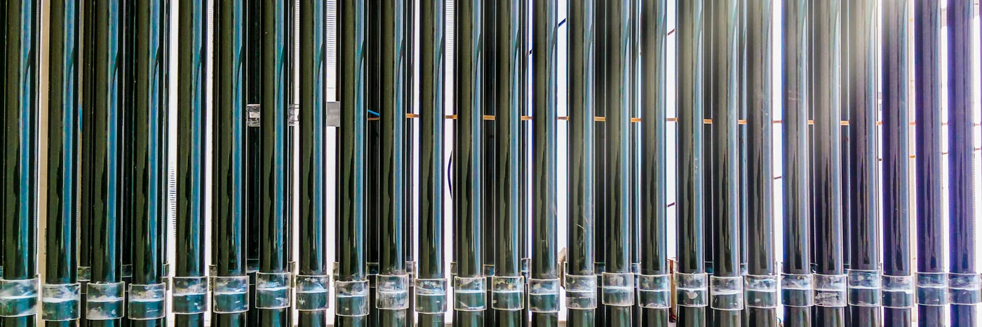 A row of tall glass photobioreactor tubes used to grow algae, lit from behind.