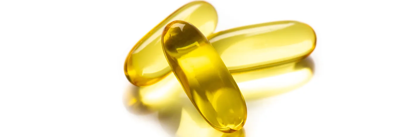 Two golden omega-3 softgel capsules photographed close up on a white surface.
