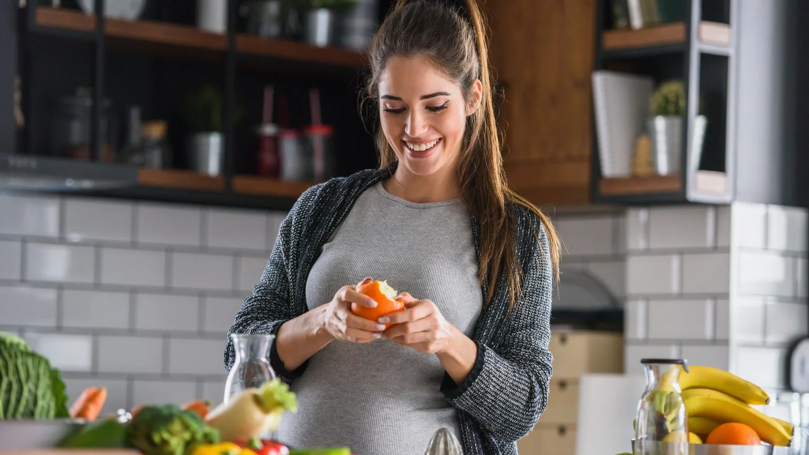A pregnant woman preparing fresh vegetables and fruit at a kitchen counter.
