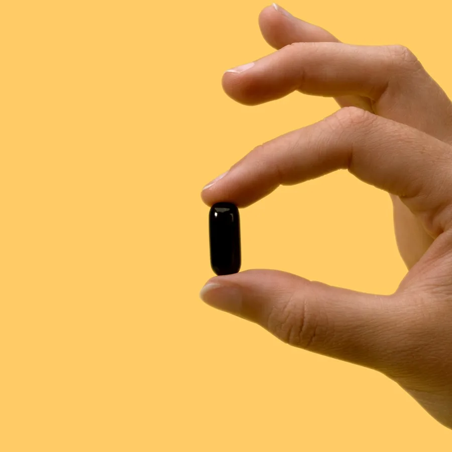 A single small iwi Omega-3 softgel held between finger and thumb, showing its size.